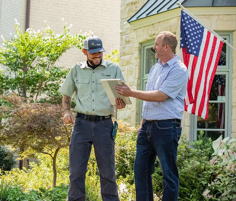 A TreeTech employee discussing plans with a smiling customer in front of a house